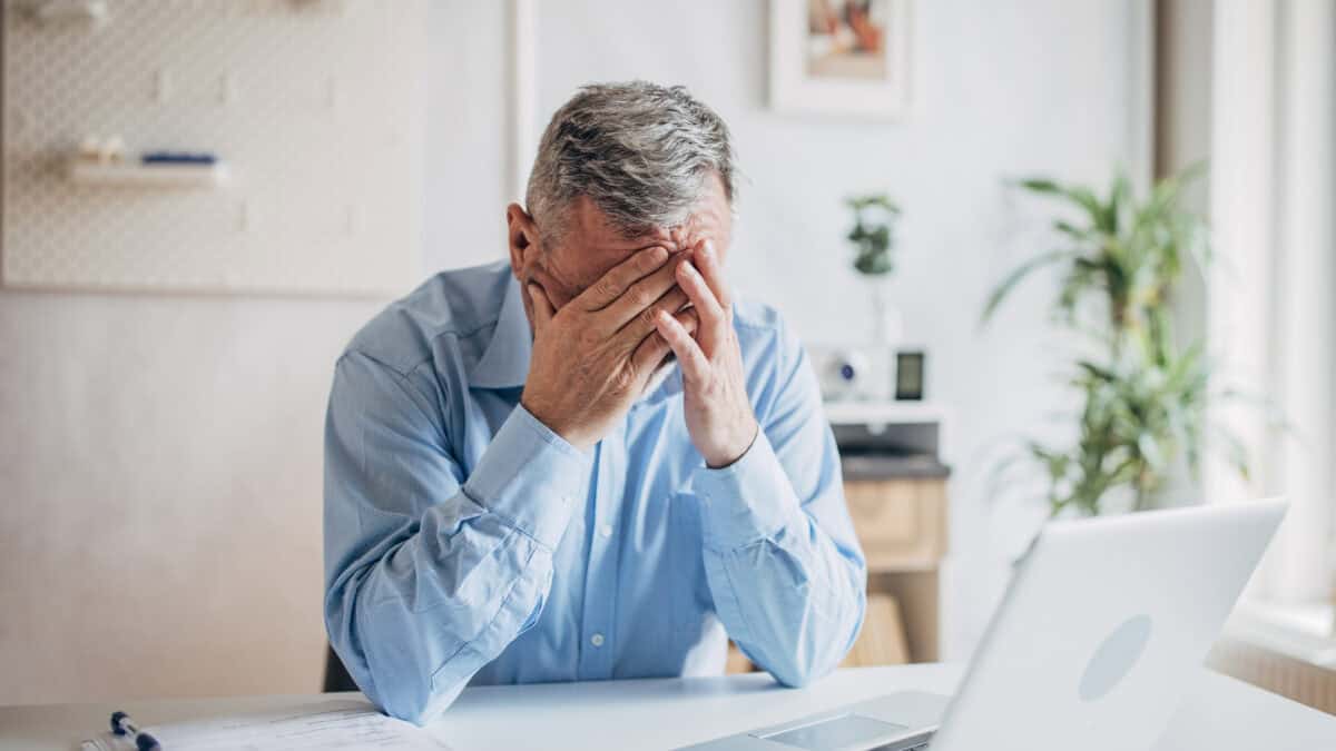 Devastated man with his hands to his head as his laptop is open.