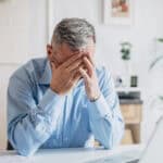 Devastated man with his hands to his head as his laptop is open.