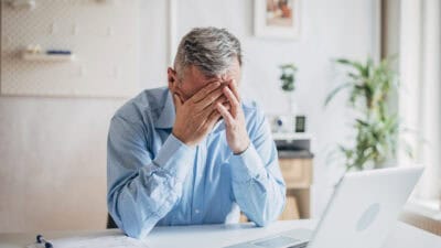 Devastated man with his hands to his head as his laptop is open.