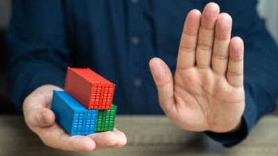 Model shipping containers in one hand, with the other hand doing a halt gesture.