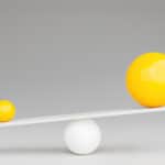 One large yellow sphere on one side of a white seesaw, with a small yellow sphere on the other side.