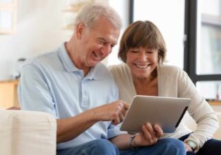 A happy couple looking at an iPad feeling great as they watch the Challenger share price rise